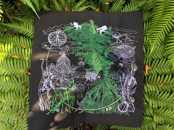 The Cloth showing black and green illustration laying on a green fern